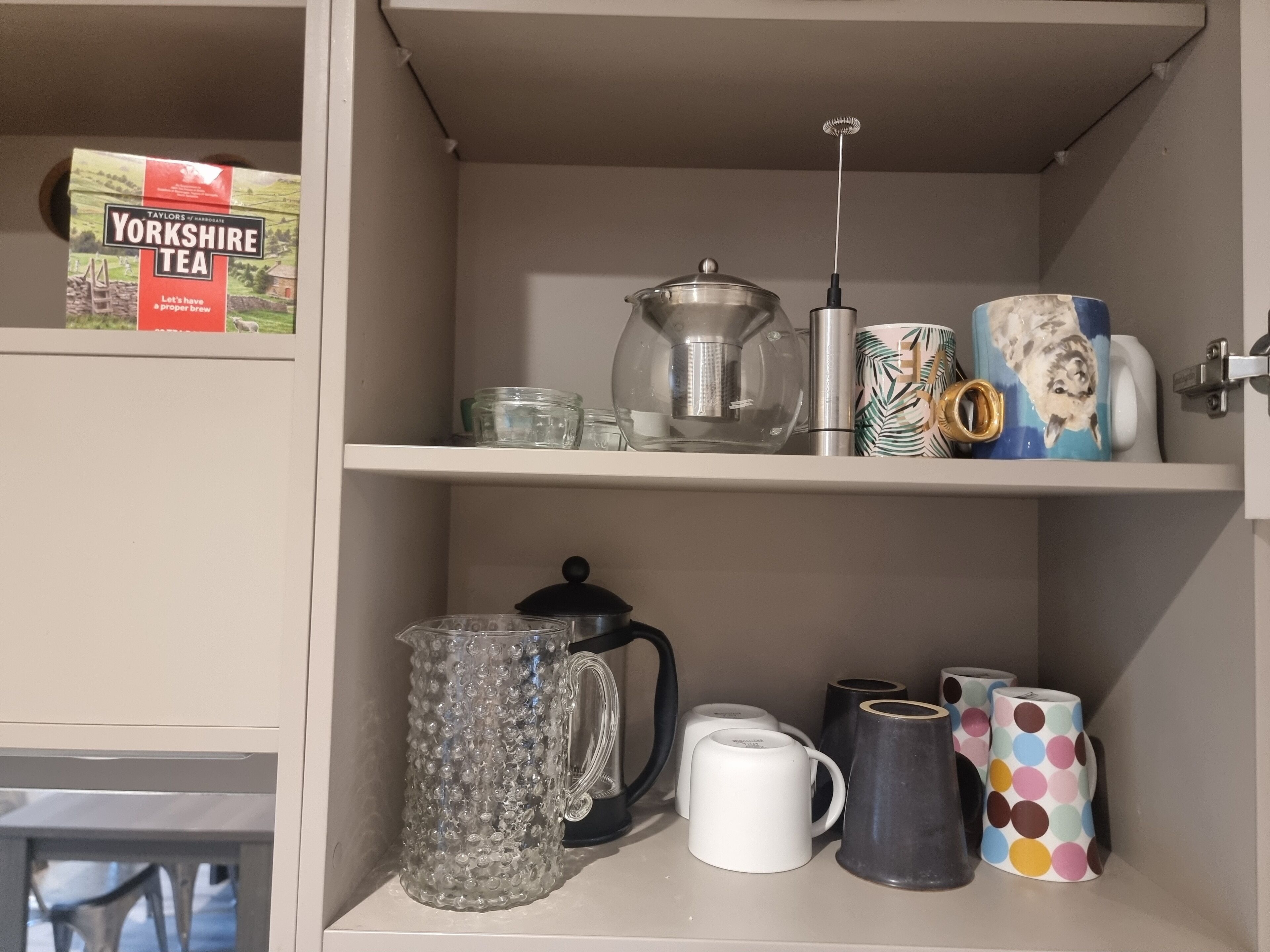 Un meuble de cuisine contenant des boîtes à thé, une bouilloire, des tasses et une machine à café.