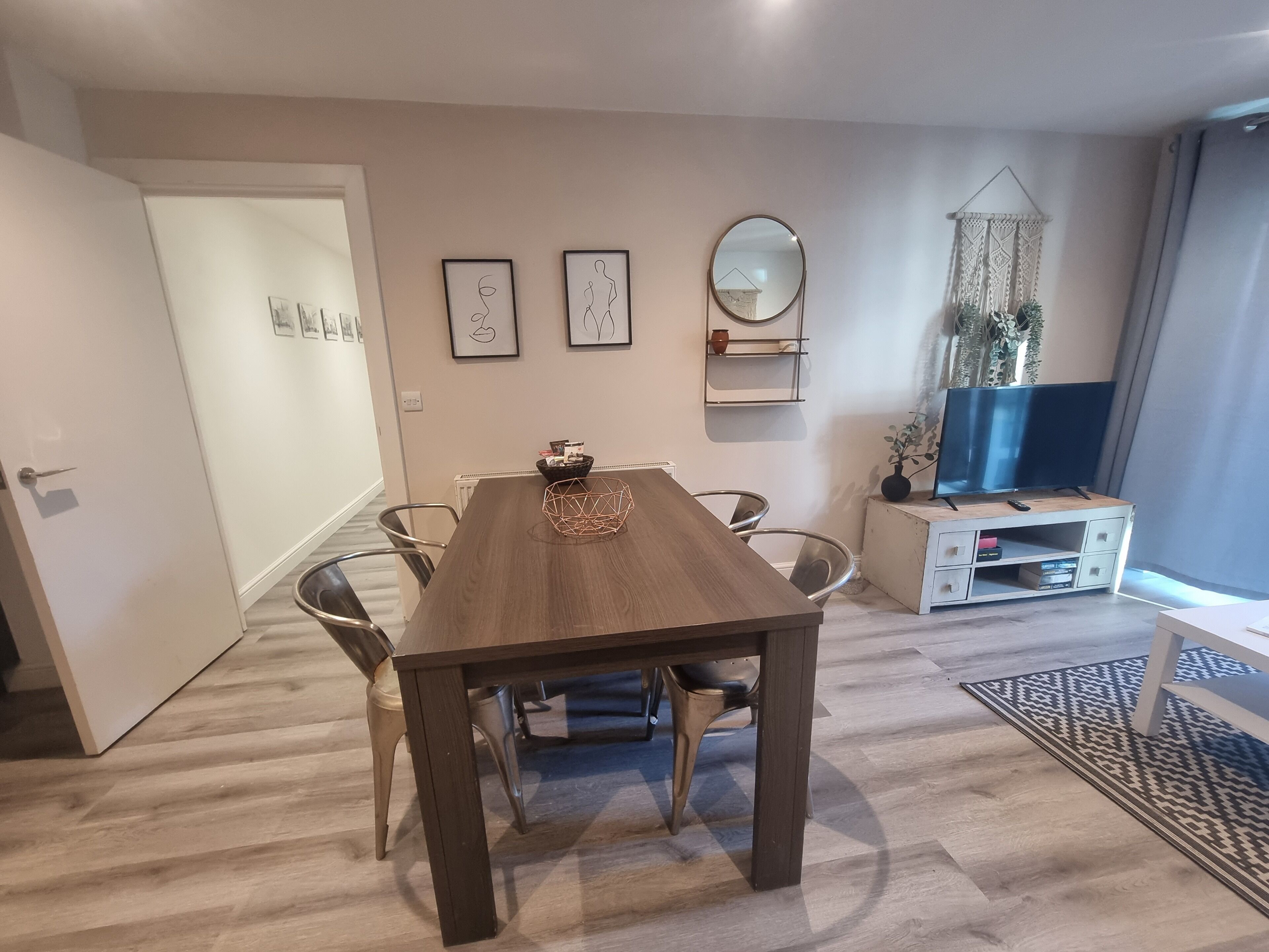 A dining area with a wooden table, chairs, a white cabinet with a TV, and a decorative mirror.
