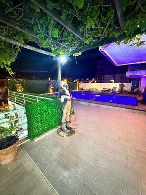 A nighttime outdoor area with a statue, a pool, and lounge chairs. - Pacific Hotel (Cesme)