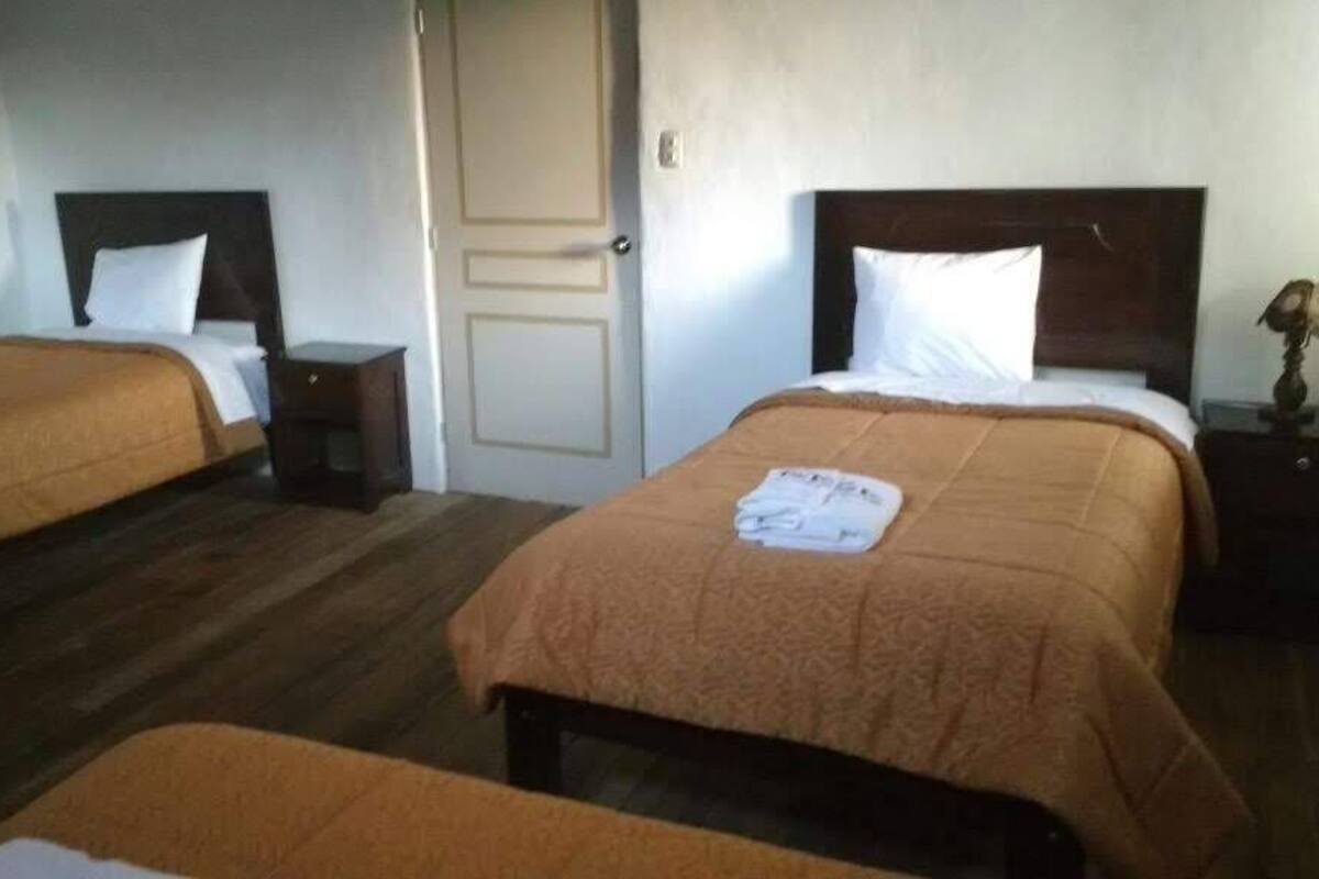 A hotel room with two single beds, each with a wooden headboard, a bedside table, and a lamp.