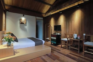 A wooden-floored room with a bed, a desk, a chair, a TV, and a small table with a vase of flowers. - Xiangxingli Inn (Tengchong Heshun Ancient Town Branch) (Tengchong)