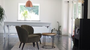 Una sala de estar moderna con un piano, un sillón marrón, una mesa redonda de madera y un amplio ventanal con luz natural.