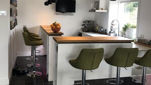 Una cocina moderna con una isla central, taburetes de bar, un televisor de pantalla plana y un ventanal que proporciona luz natural.