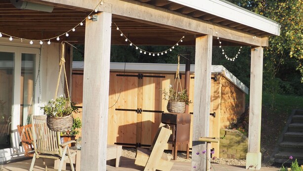 Una terraza de madera con pérgola, luces colgantes y macetas suspendidas.