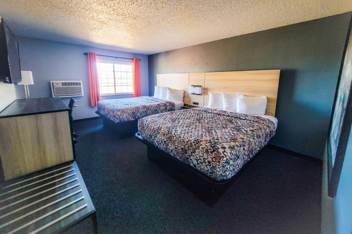 Une chambre d’hôtel avec deux lits, un bureau, un appareil de climatisation et une fenêtre avec des rideaux.