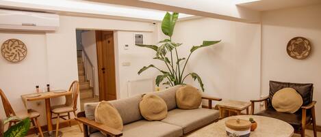 Uma sala de estar moderna com um sofá bege, cadeiras de madeira, uma mesinha e uma planta grande.