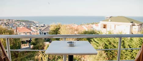 A balcony with a table and two cushioned chairs overlooking a coastal town.