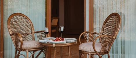 A dining area with wicker chairs and a table, a glass door leading inside, and a small garden area with plants.