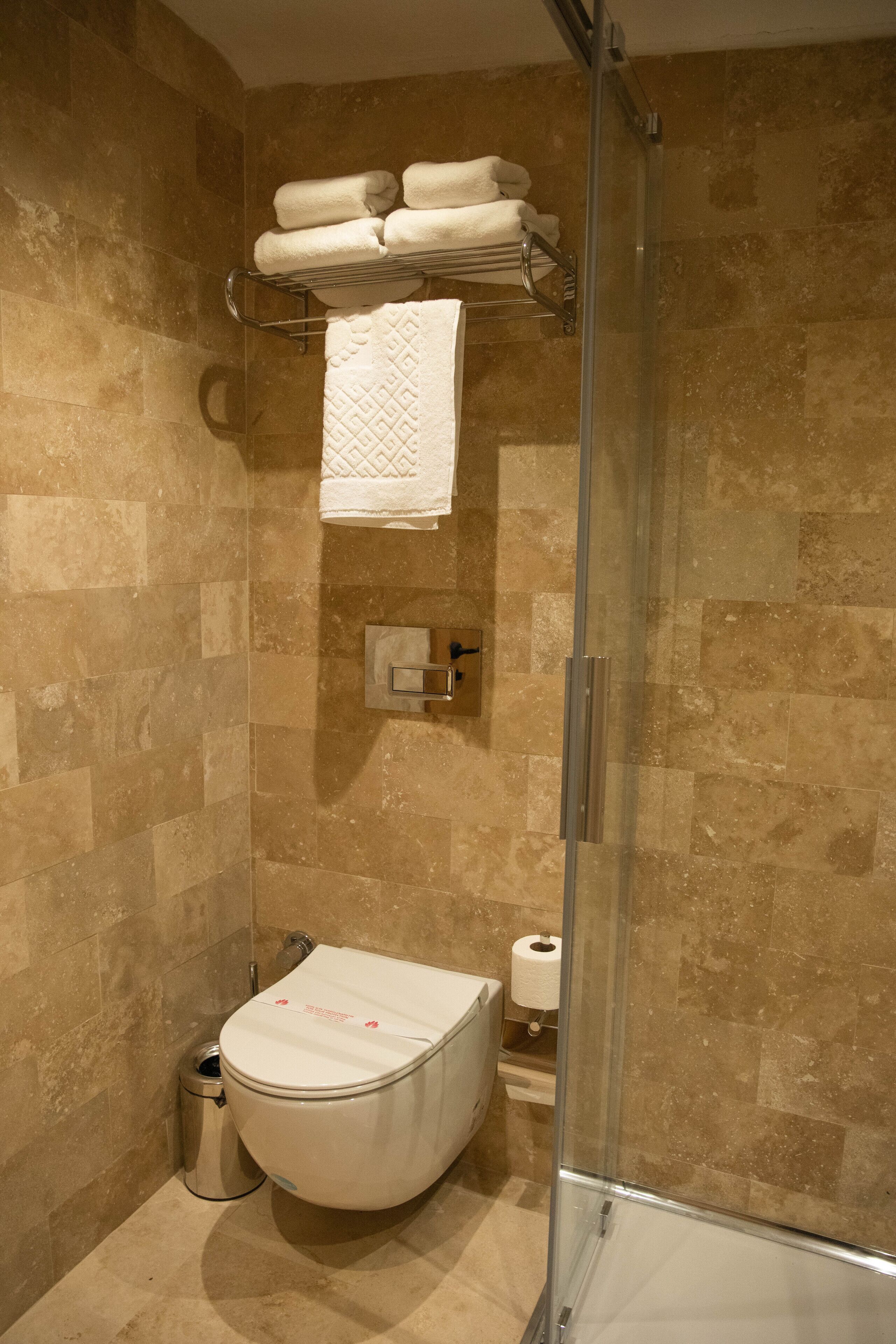 A bathroom with a glass-enclosed shower, a toilet, and a towel rack with folded towels.