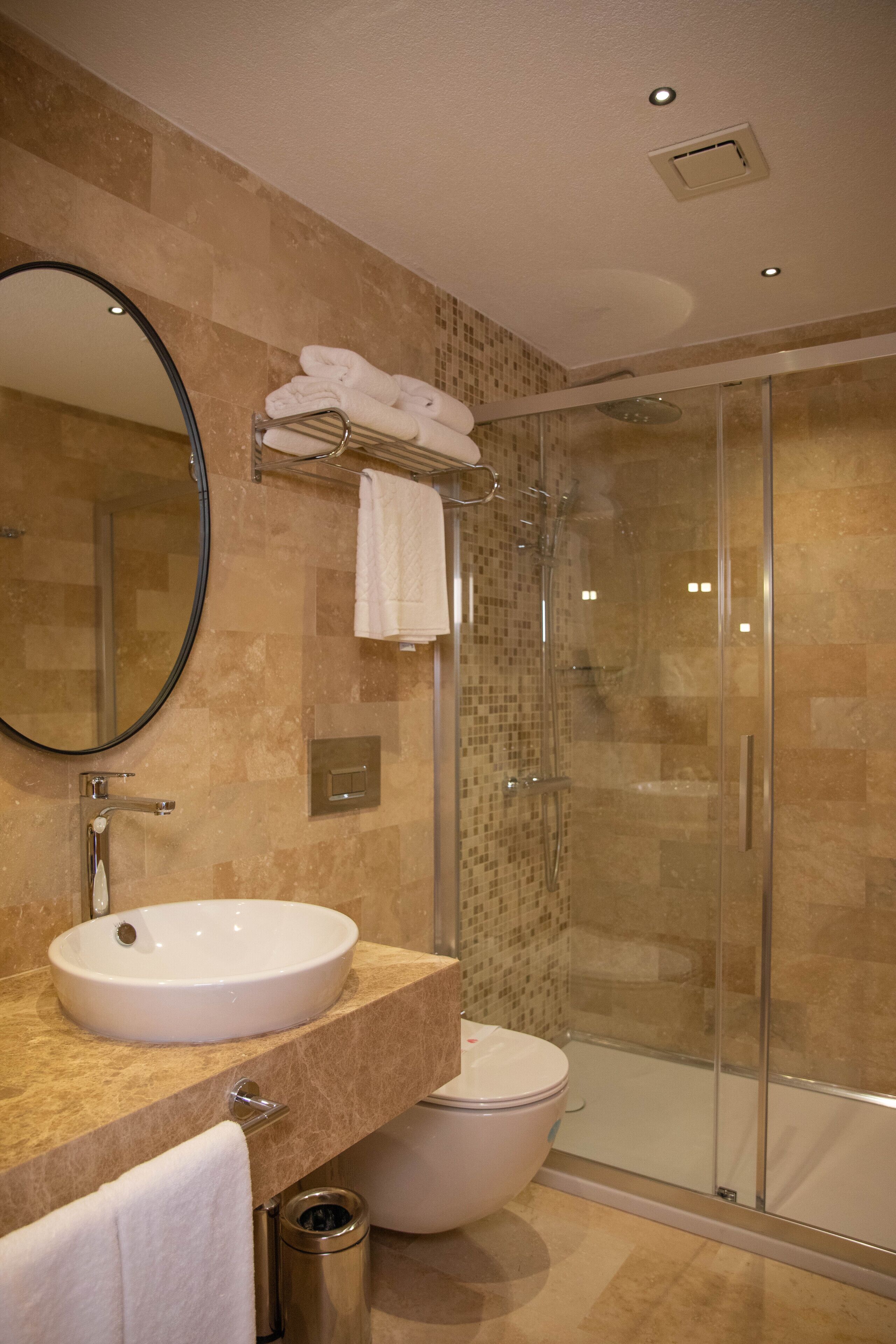 Une salle de bain moderne avec un lavabo rond, des toilettes, une douche en verre et un miroir.