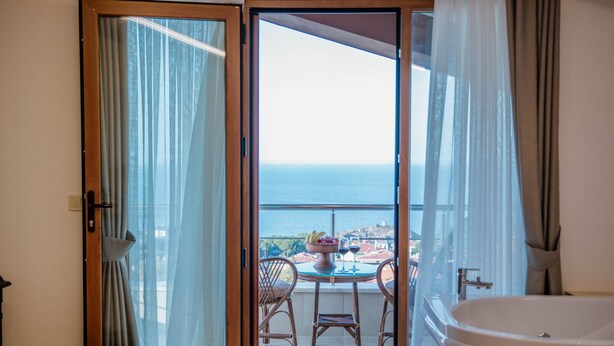 A balcony with a view of the sea, a table with chairs, and a bathtub.