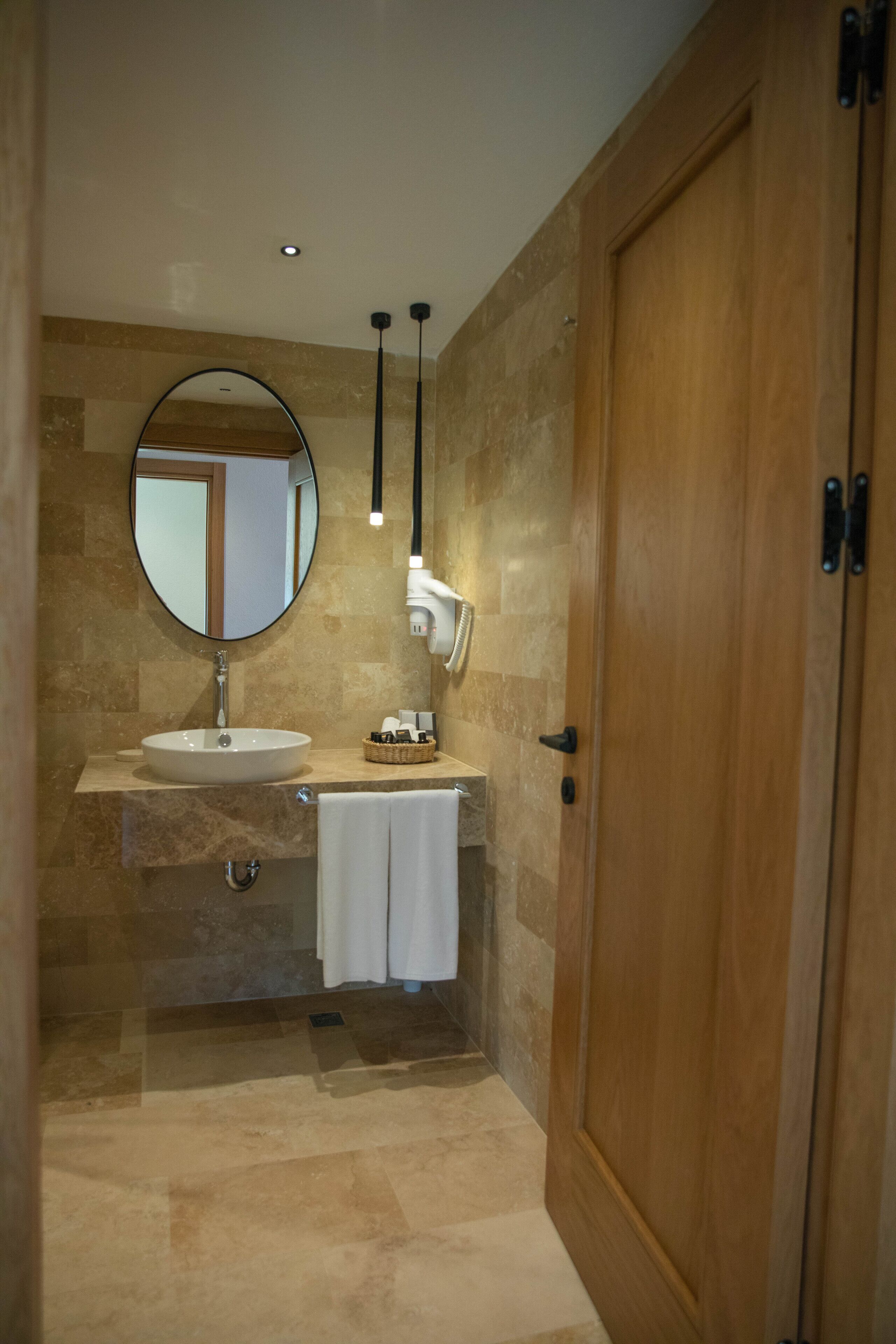 Un baño con lavamanos, espejo, toallero y puerta de madera.