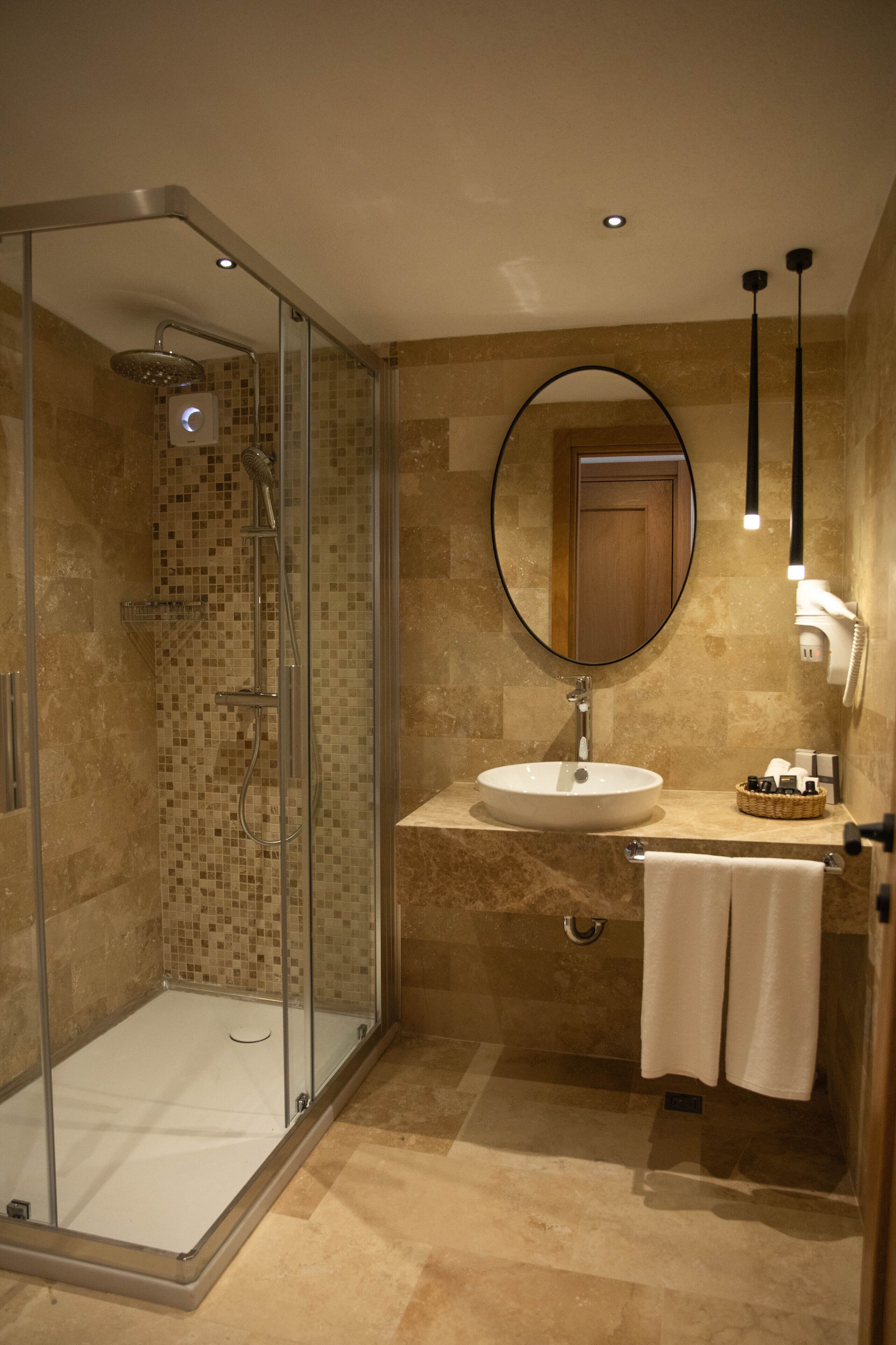 Une salle de bain moderne avec une douche à parois de verre, un miroir rond, un lavabo et un porte-serviettes.