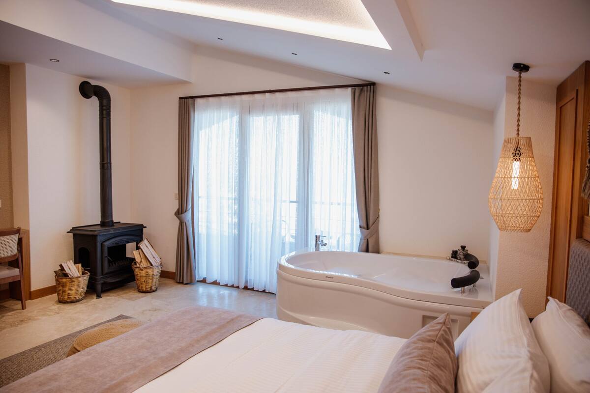 Une chambre moderne avec un grand lit, une cheminée intégrée, une baignoire et une grande fenêtre avec des rideaux.