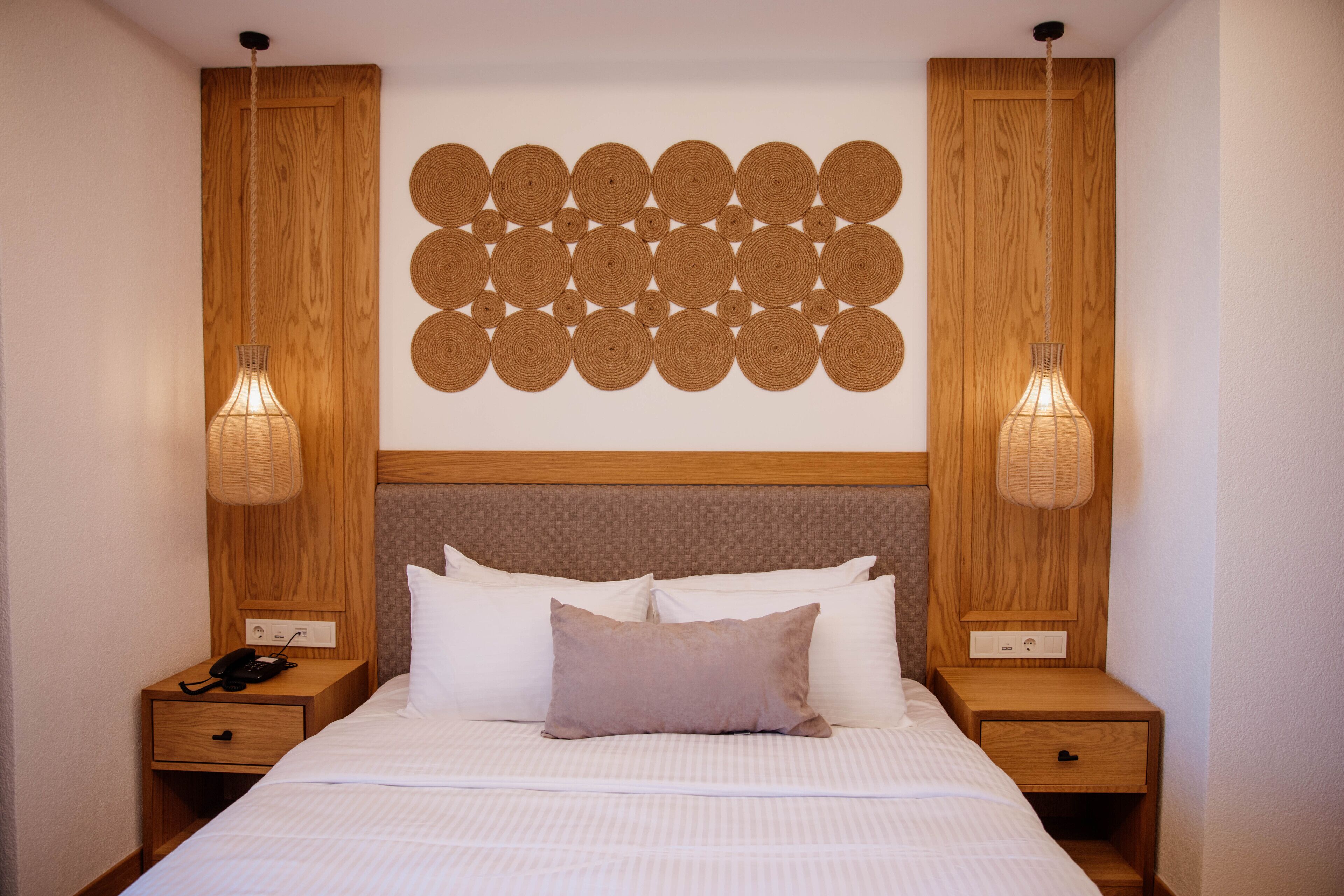 A neatly arranged hotel room with a large bed, two bedside tables, a wall-mounted circular decoration, and two wall-mounted lamps.