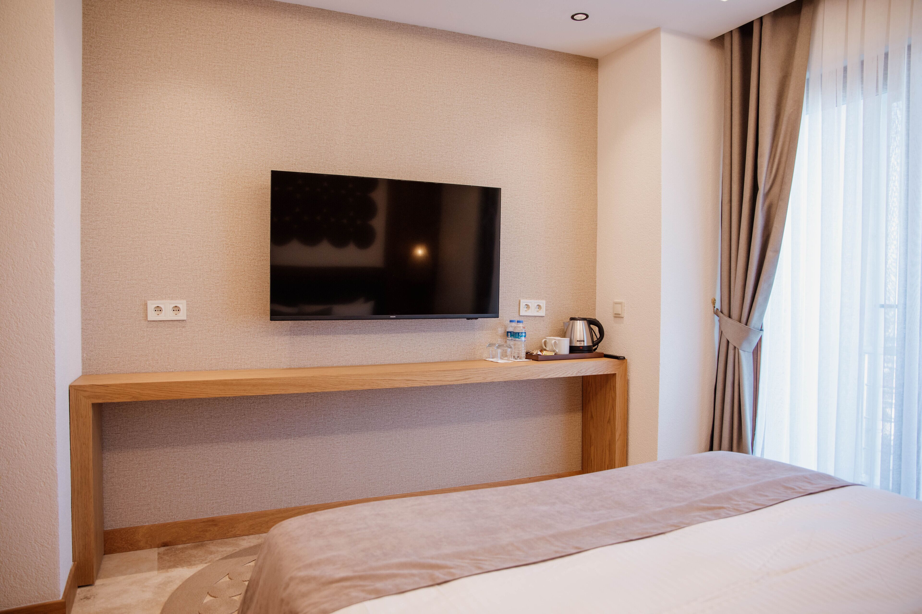 A hotel room with a bed, a TV mounted on the wall, a coffee maker, and a window with curtains.