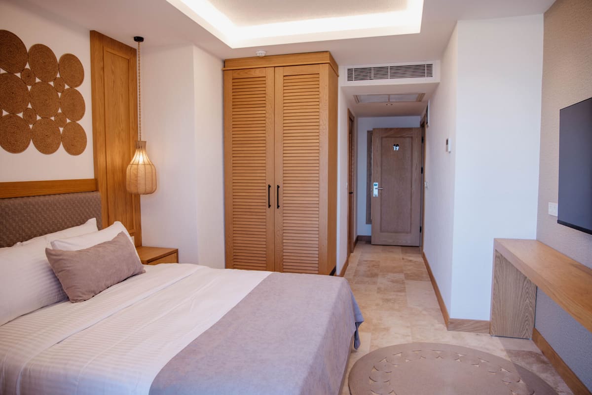Une chambre à coucher comprenant un lit, une armoire, un téléviseur et un couloir menant à une autre pièce.