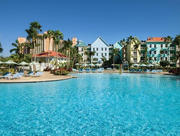 Relax by the pool surrounded by lounge chairs and umbrellas, with a clear view of the hotel buildings.