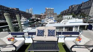 A rooftop terrace with two lounge chairs, a small table, and a view of the marina with boats and buildings. - Endless Summer: Oceanside Views (Boston)