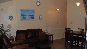 A living room with a sofa, a coffee table, a dining table with chairs, and a painting on the wall. - 123 West Harbor Condo B - Beautiful Condo in the harbor with spacious deck (Port Mansfield)