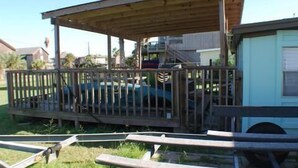 A covered outdoor area with a wooden fence, a vehicle, and a building in the background. - 116 Southshore - Cute little hideaway, ready for the all around fishing (Port Mansfield)