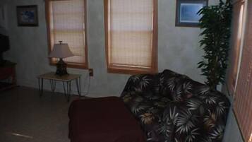 Ein Wohnzimmer mit einer Couch, einer Lampe und zwei Fenstern mit Jalousien.