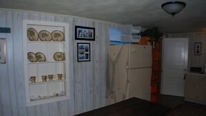 A room with a wooden bench, a refrigerator, and a wall with framed photos and decorative plates. - 116 Southshore - Cute little hideaway, ready for the all around fishing (Port Mansfield)