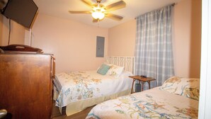 Un dormitorio con dos camas, ventilador de techo, televisor y cómoda de madera.