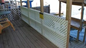 Een houten terras met een wit, geperforeerd privacy scherm, een blauwe tafel en een houten stoel.