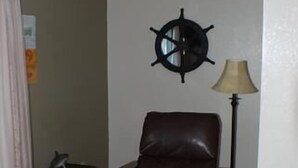 Een woonkamer met een bruine leren fauteuil, een bijzettafeltje, een lamp en een aan de muur bevestigde decoratie van een schipsschroef.