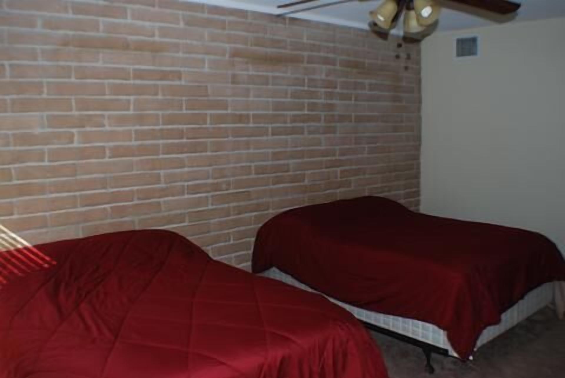 A room with two beds, a brick wall, and a ceiling fan.