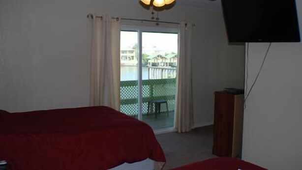 Een hotelkamer met een plafondventilator, een aan de muur bevestigde televisie en een balkon met uitzicht op gebouwen.