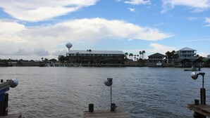 A waterfront view with a dock, a large building with multiple stories, and several palm trees.