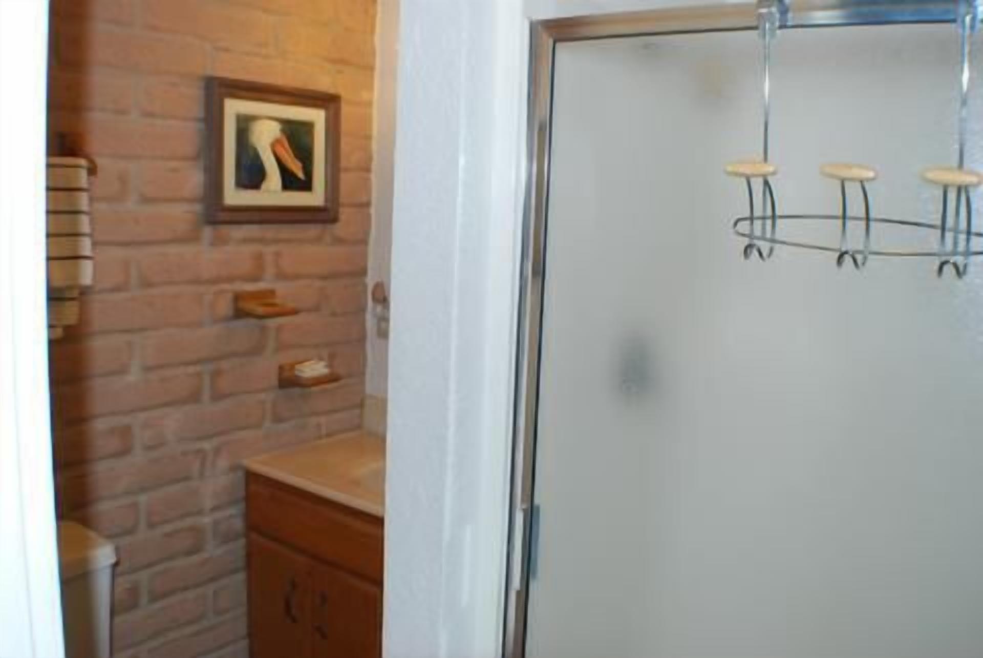 Un baño con pared de ladrillo, un cuadro enmarcado, un mueble de madera y un box de ducha de vidrio con grifo.