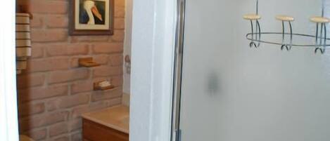 A bathroom with a brick wall, a framed picture, a wooden cabinet, and a glass shower enclosure with a faucet.