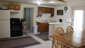 A compact kitchen with wooden cabinets, a microwave, and a dining area with a wooden table and chairs.