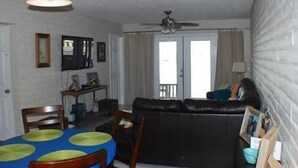 A living room with a black leather sofa, a dining table with green placemats, and a ceiling fan. - Fabulous Fisherman's Condo! (Port Mansfield)