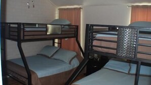 A room with two bunk beds, each with a pillow and a blanket. There is a small table and a chair in the corner. - Fabulous Fisherman's Condo! (Port Mansfield)