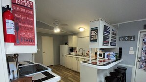 A compact kitchen with a central island, white cabinets, a microwave, and a sink. There are bar stools and a fire extinguisher visible.