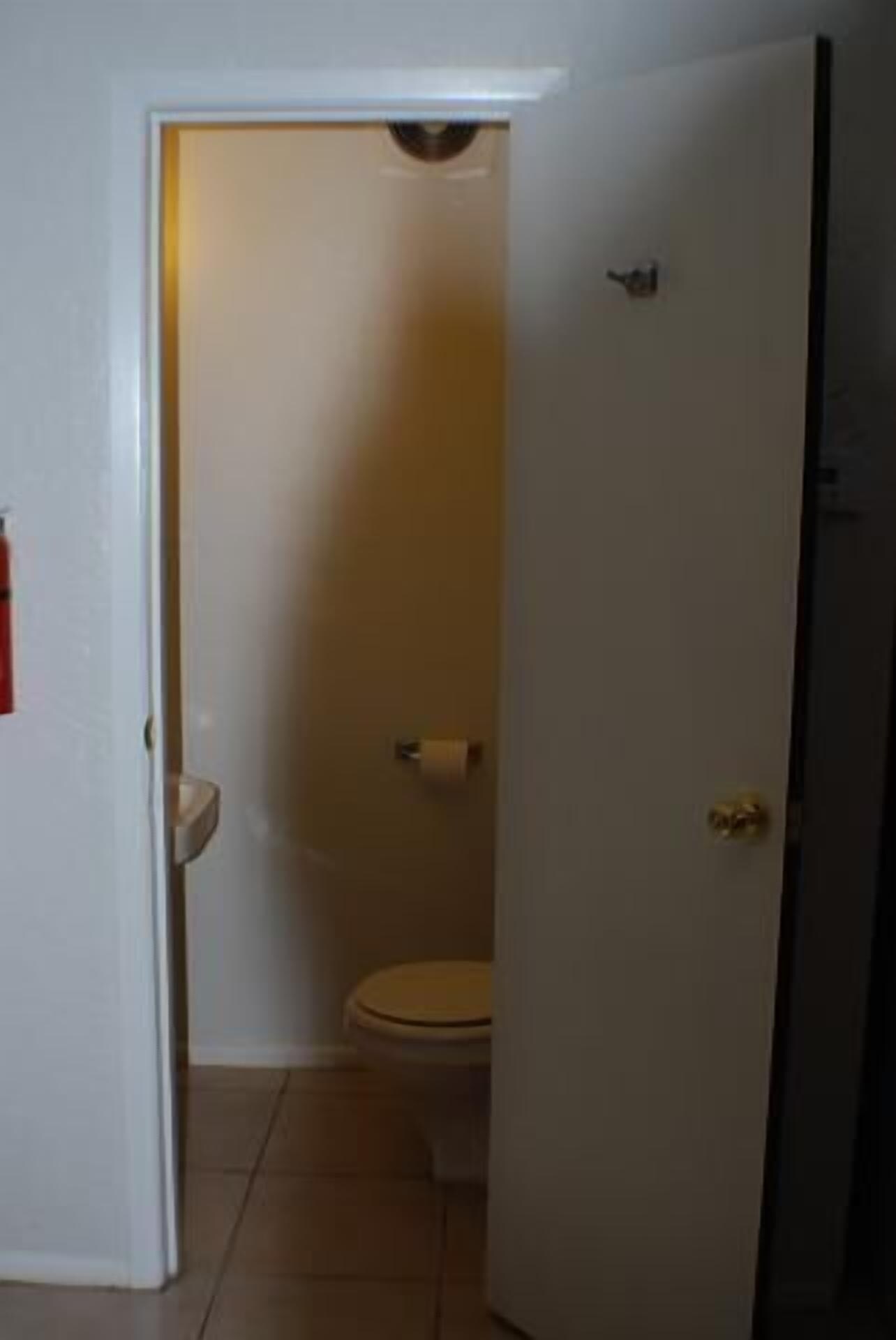 A small, narrow bathroom with a toilet and a roll of toilet paper on the wall.