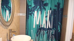 Une salle de bain avec un lavabo blanc, un miroir et un rideau de douche orné de motifs de palmiers.