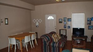 Un salon comprenant un canapé, un téléviseur, une table à manger avec des chaises et une porte avec une fenêtre.