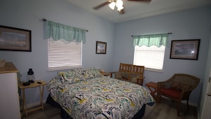 A bedroom with a bed, two windows with curtains, a chair, a small table, and a ceiling fan. - 513 Laguna D - Right on the Water, Great Common Area (Port Mansfield)