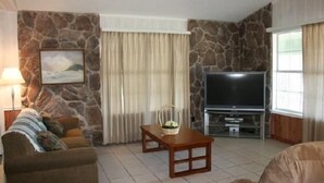 Uma sala de estar com parede de pedra, televisão, sofá e mesa de centro.