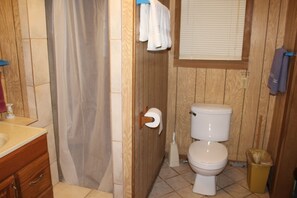 A bathroom with a wooden vanity, a toilet, and a shower curtain. - 601 Baffin - Cozy little cottage! Screened in front porch. (Port Mansfield)