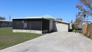 A single-story house with a covered porch, a garage, and a visible chimney. - 601 Baffin - Cozy little cottage! Screened in front porch. (Port Mansfield)