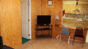 A compact living space with a television on a wooden stand, a dining area with a bar counter, and a kitchen with wooden cabinets. - 601 Baffin - Cozy little cottage! Screened in front porch. (Port Mansfield)