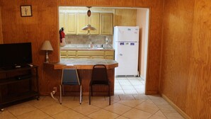 A small kitchen with wooden cabinets, a white refrigerator, a sink, and a dining area with two chairs. - 601 Baffin - Cozy little cottage! Screened in front porch. (Port Mansfield)