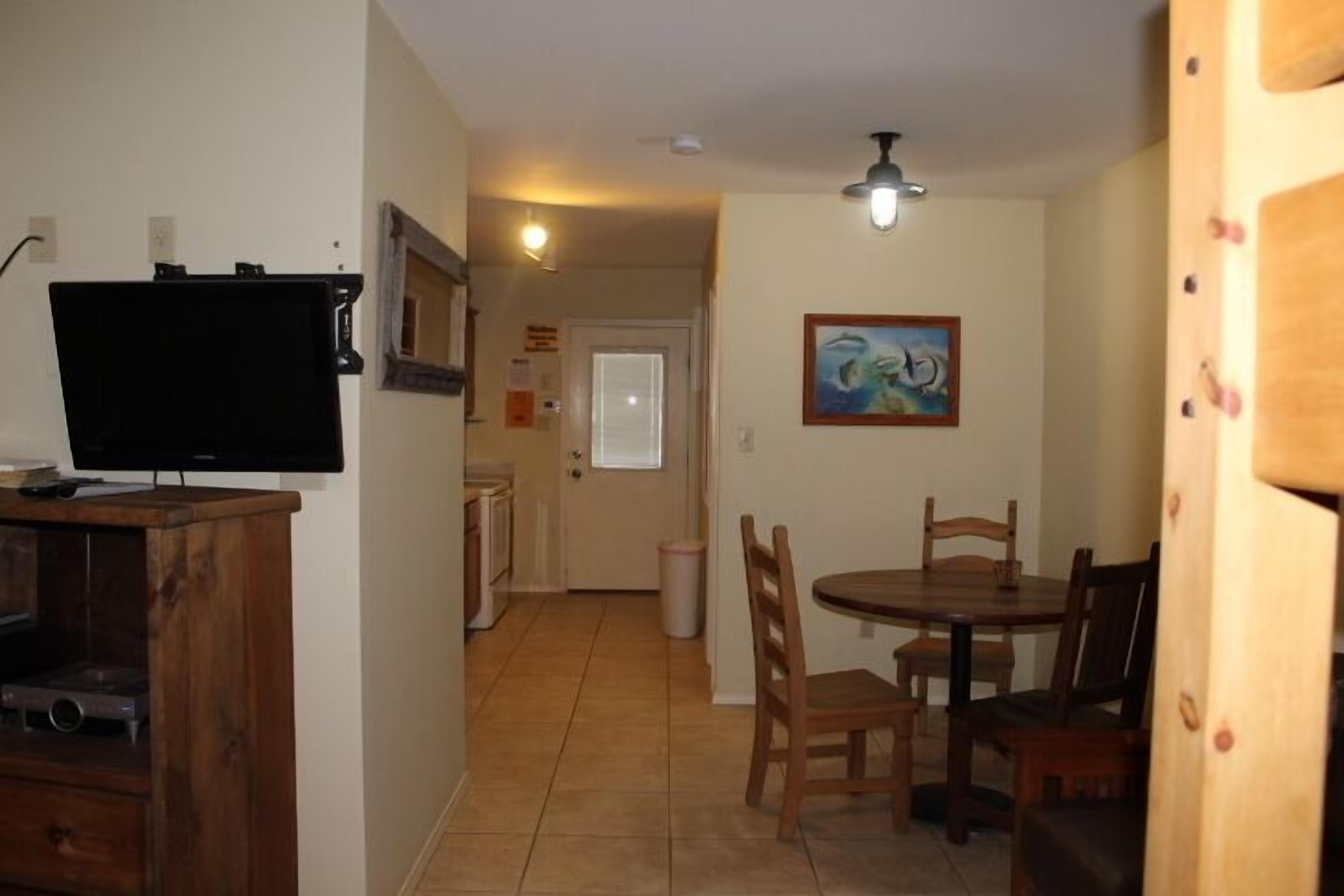 A dining area with a wooden table and chairs, a television on a wooden stand, and a ceiling fan.