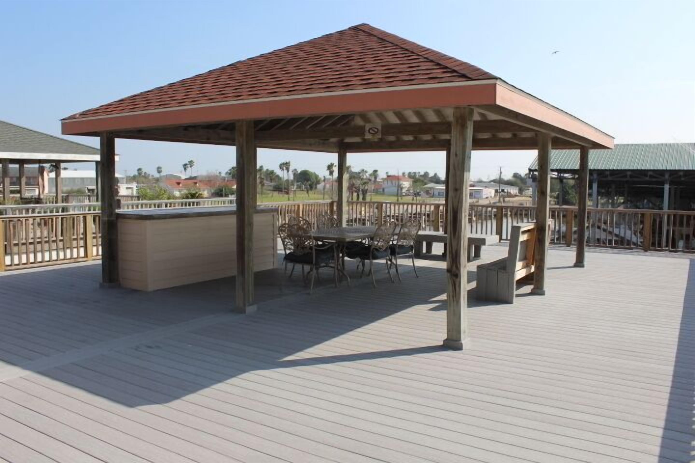 A covered outdoor area with a wooden deck, a table with chairs, and a small bar area.